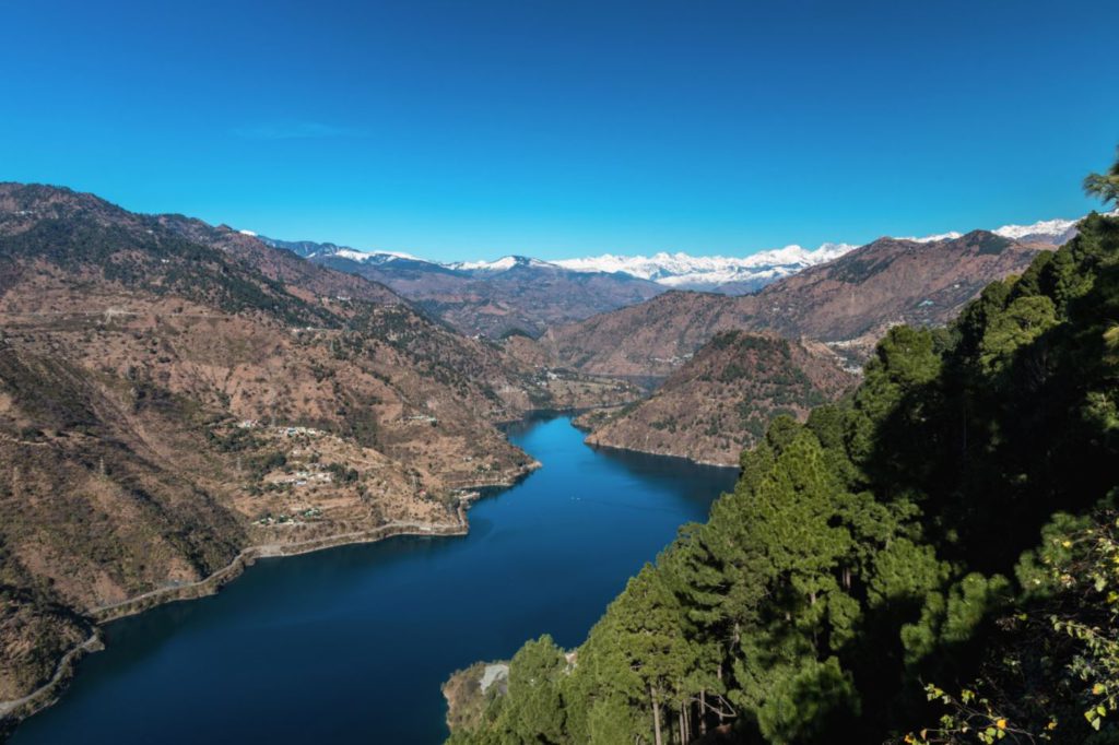 The snake shaped Chamera lake as seen from a top view point with snow covered peaks in the background